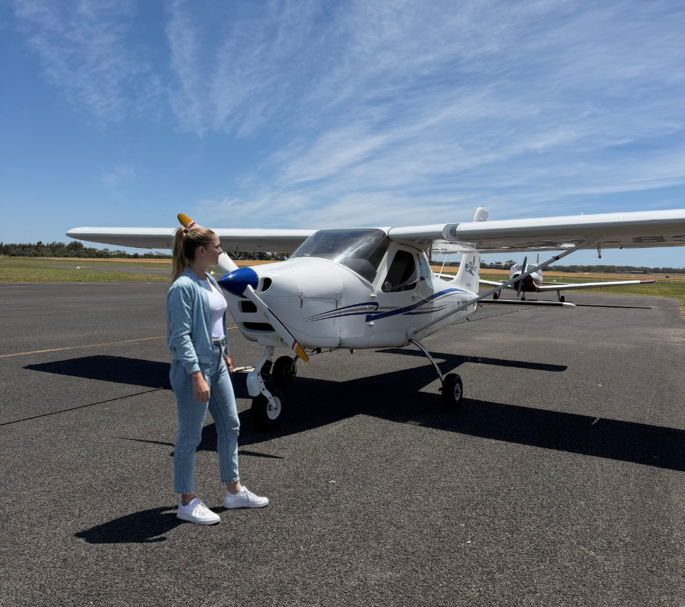 Person standing next to a small airplane on a runway with a clear blue sky.