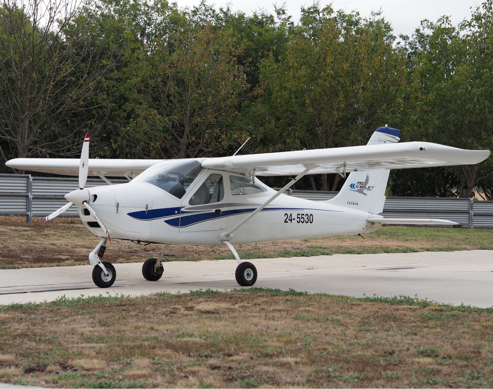 Small white airplane with blue accents on a runway with trees in the background