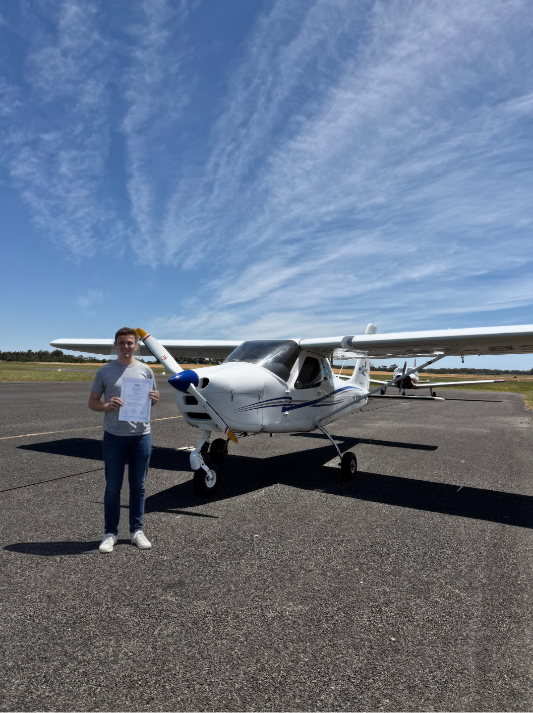 Person standing next to a small airplane on a runway with a clear blue sky.