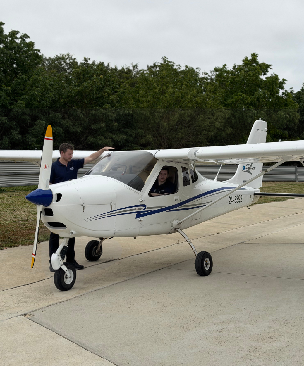 Small white airplane on a runway with a person standing next to it