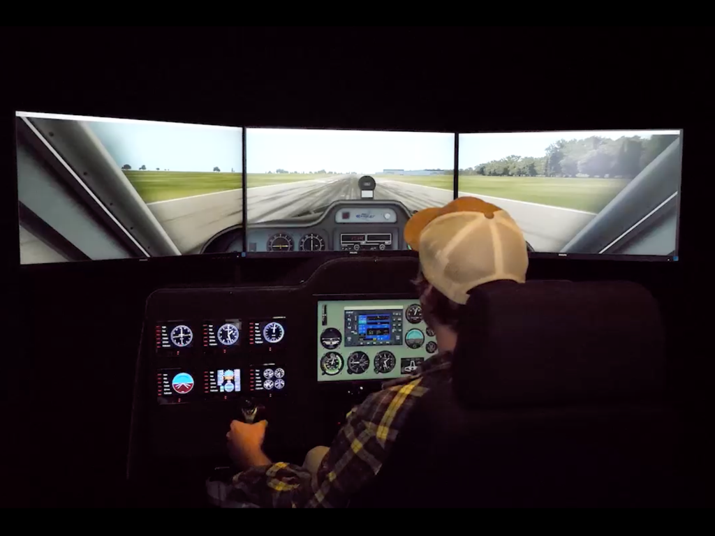 Person using a flight simulator with multiple screens displaying a cockpit view.